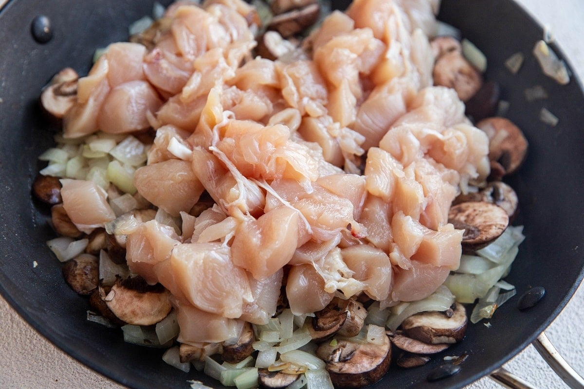 Onions, mushrooms, and raw chicken breast in a skillet.