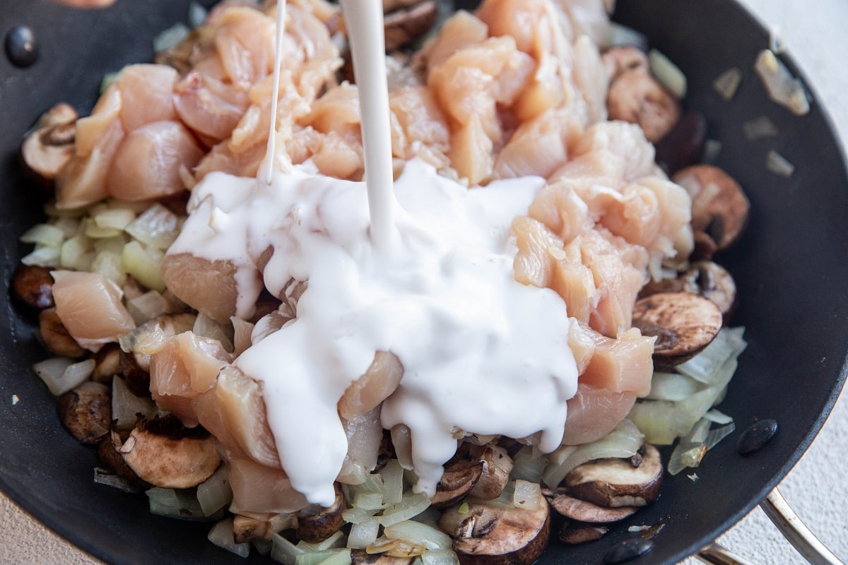 Coconut milk being poured into the large nonstick skillet with onions, mushrooms, and chicken.