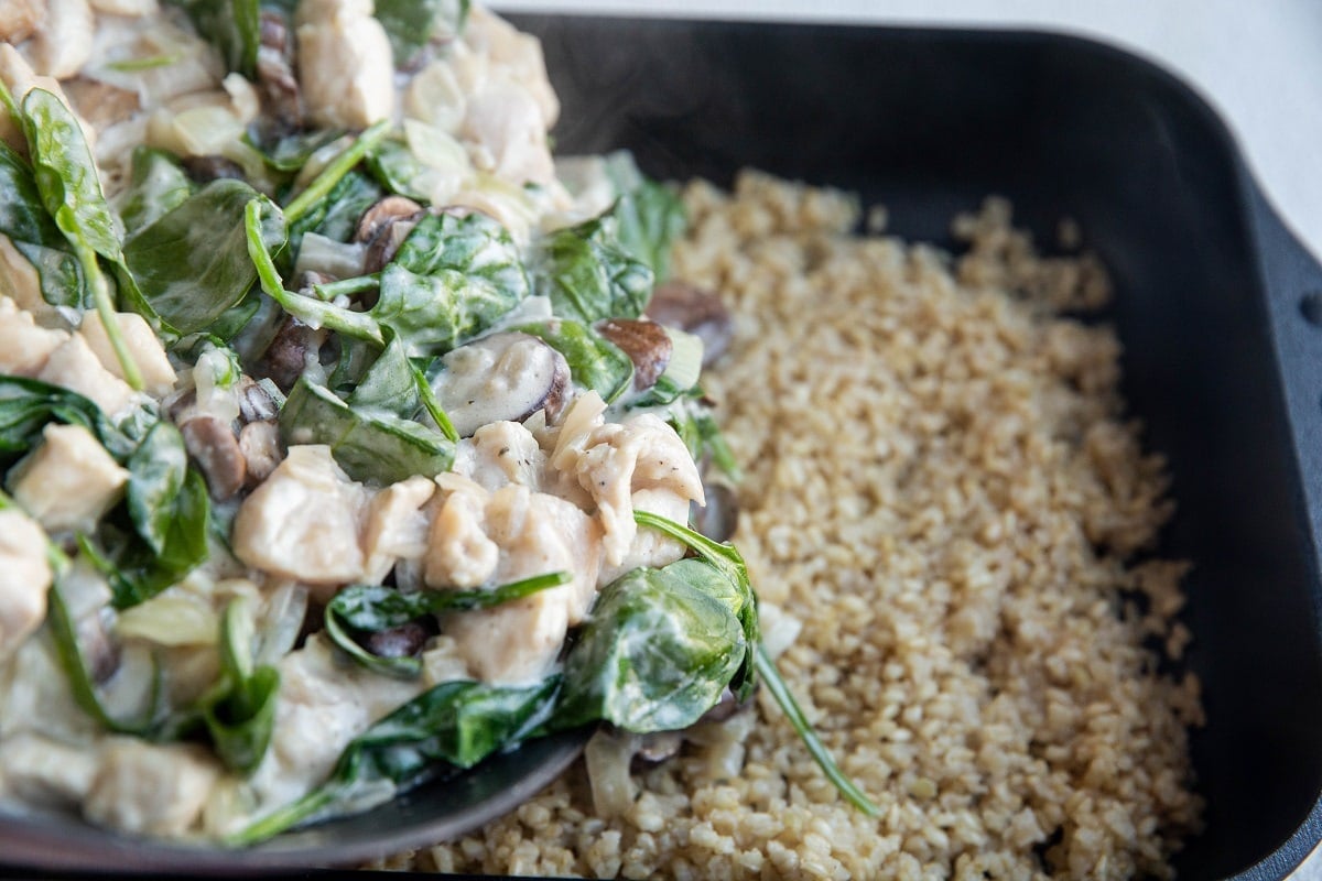 Chicken mushroom mixture being poured over the brown rice.