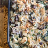 Large casserole dish full of chicken and mushroom casserole with creamy rice sitting on a rustic wood background. A wooden spoon in the casserole for serving.