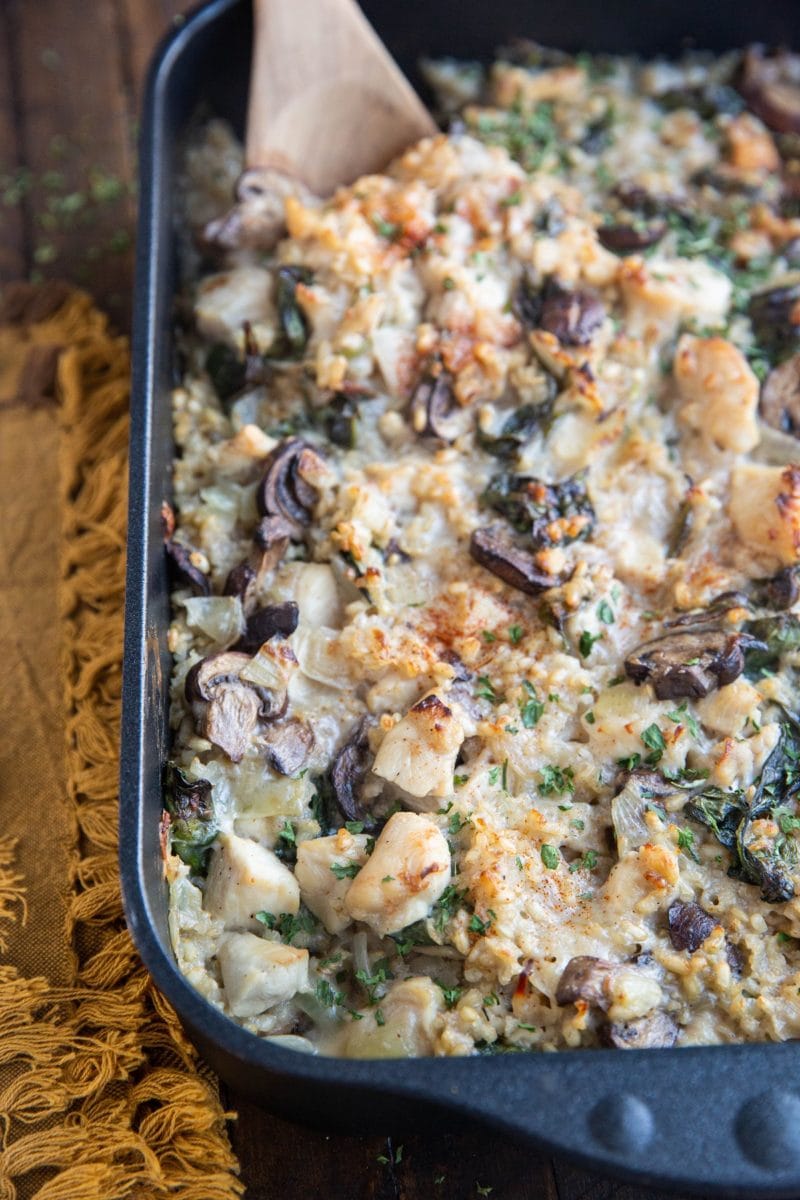 Large casserole dish full of chicken and mushroom casserole with creamy rice sitting on a rustic wood background. A wooden spoon in the casserole for serving.