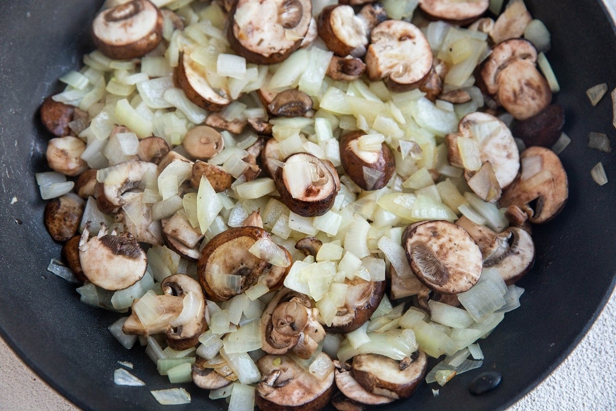 Onions and mushrooms cooking in a skillet.