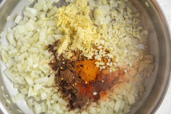 Stainless steel skillet with onions, garlic, ginger, garam masala, paprika, and more.