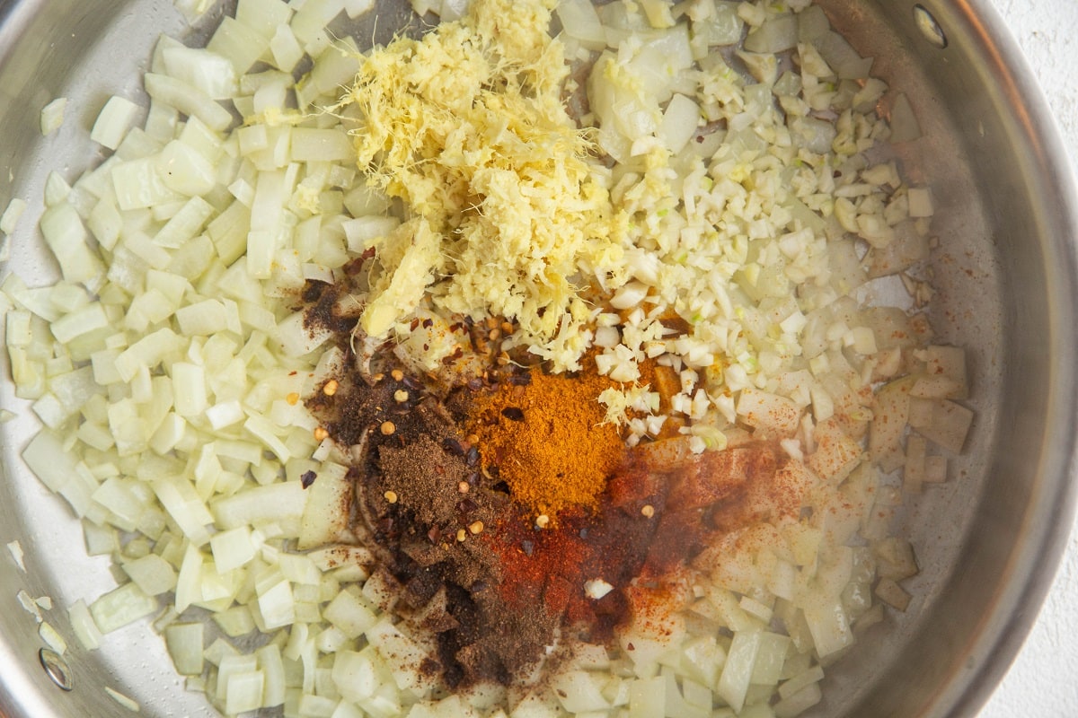 Stainless steel skillet with onions, garlic, ginger, garam masala, paprika, and more.