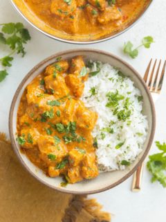 Bowl of chicken tikka masala with rice and a serving dish of chicken tikka masala with a gold fork and a gold napkin.