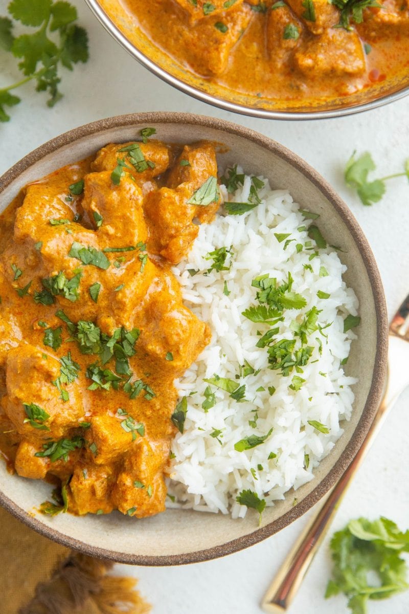 Close up top down image of bowl of chicken tikka masala and jasmine rice with chopped cilantro on top.