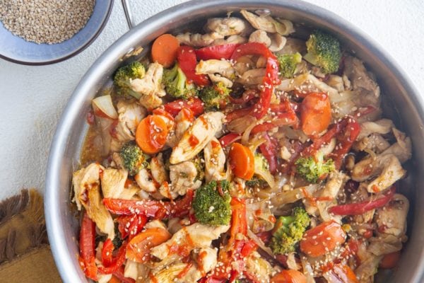 Horizontal image of finished chicken stir fry in the stainless steel skillet.