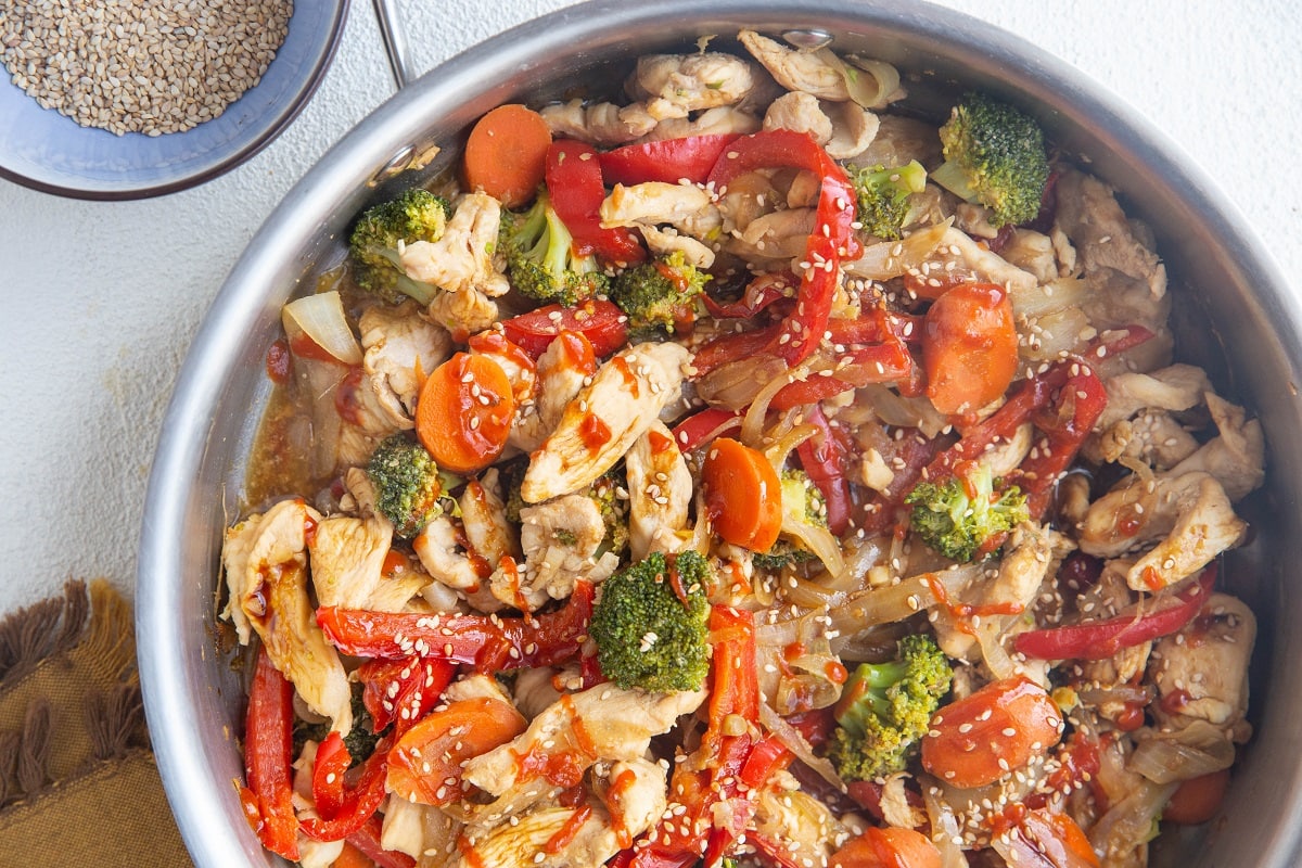 Horizontal image of finished chicken stir fry in the stainless steel skillet.