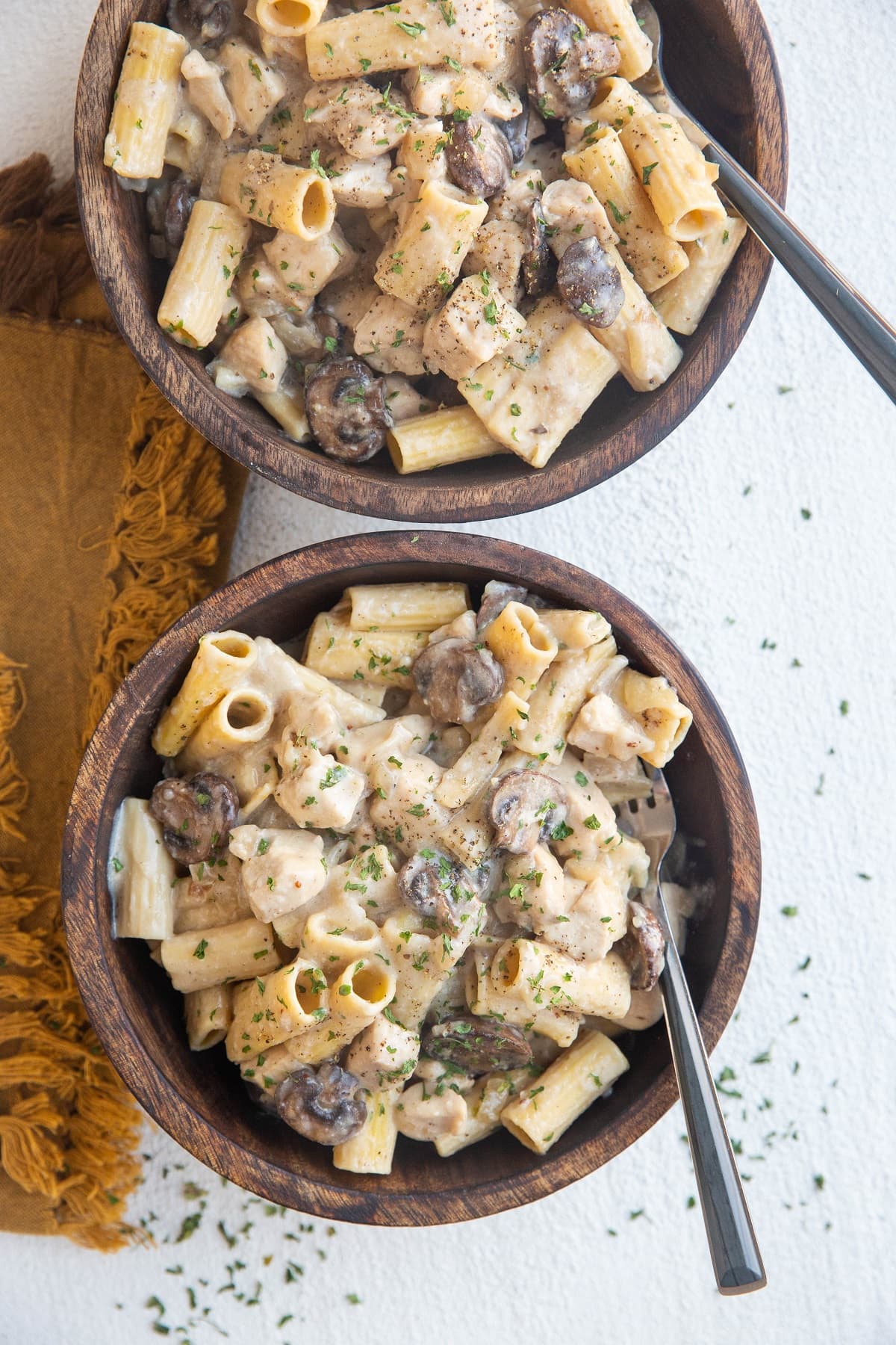 Two wooden bowls of chicken stroganoff with noodles and two wood inlay forks.