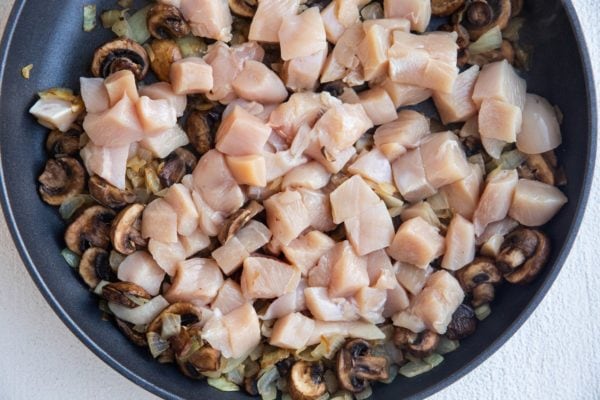 Chicken, mushrooms, and onions cooking in a skillet.