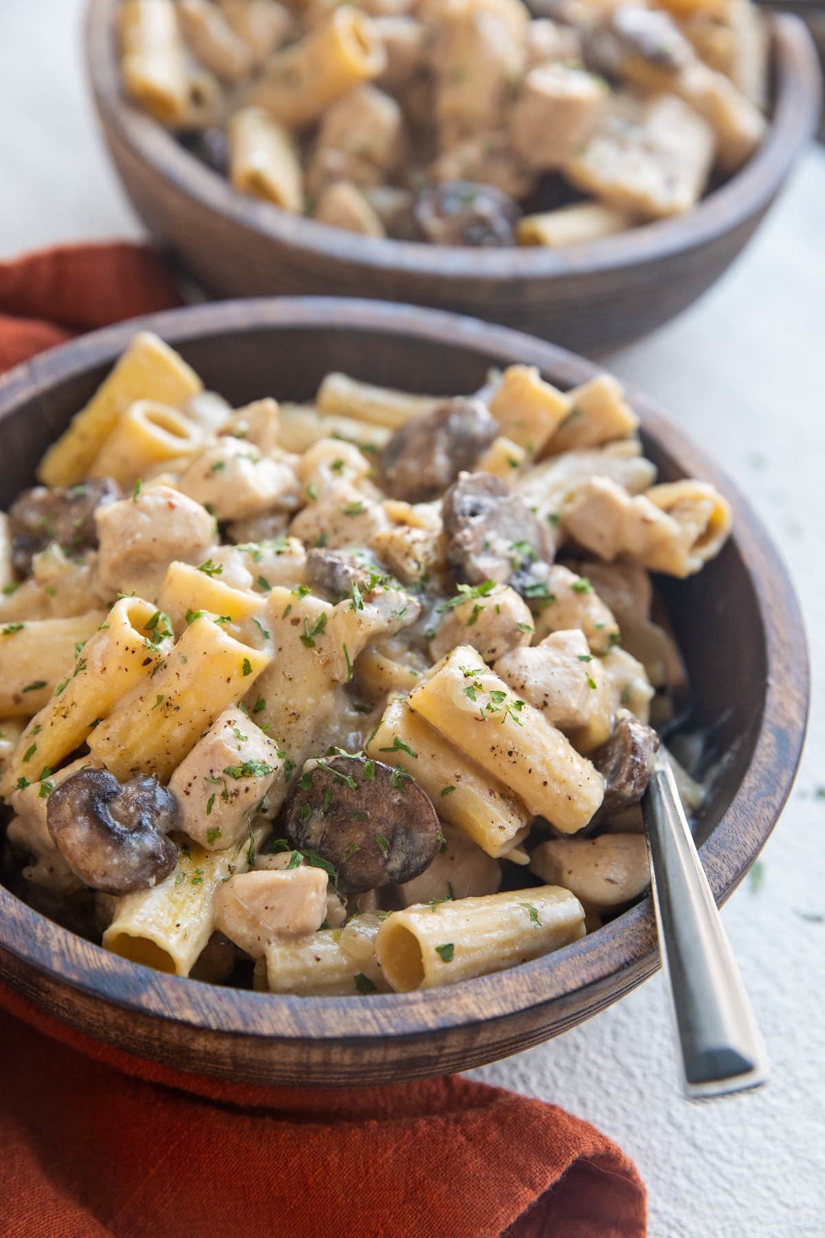 Two wooden bowls full of chicken stroganoff with a red napkin to the side.