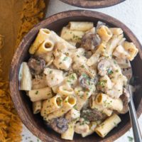 Top down two wooden bowls of chicken stroganoff with a golden napkin to the side.