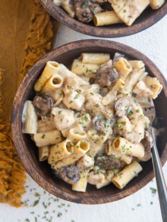 Top down two wooden bowls of chicken stroganoff with a golden napkin to the side.