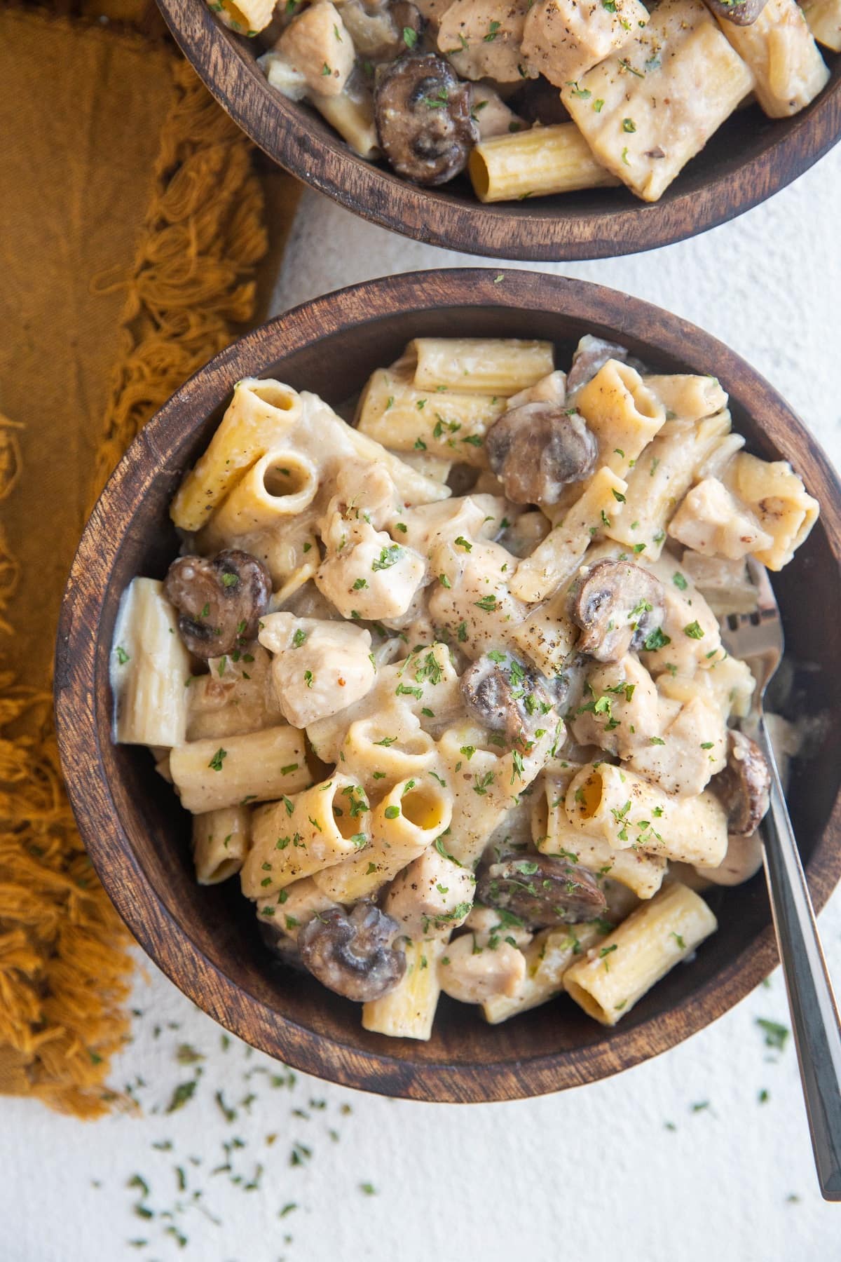 Top down two wooden bowls of chicken stroganoff with a golden napkin to the side.