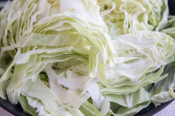 Raw sliced cabbage in a skillet with onions to be cooked.