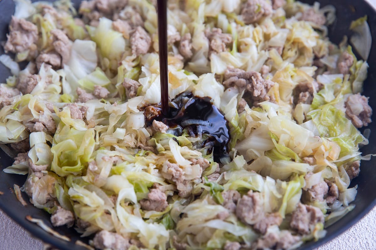 Pouring coconut aminos in the skillet with ground turkey, cabbage, and onions.