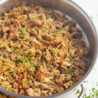 Stainless steel skillet full of ground turkey and cabbage with sriracha drizzled on top and sprinkled with parsley