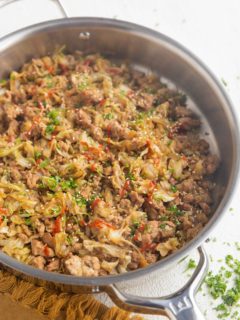 Stainless steel skillet full of ground turkey and cabbage with sriracha drizzled on top and sprinkled with parsley