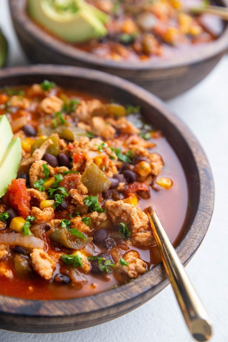 Angled photo of two wood bowls of taco soup with gold spoons.