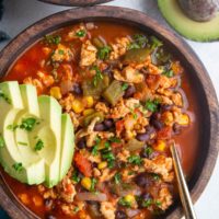Two large wooden bowls of ground turkey taco soup with sliced avocado on top, ready to eat.