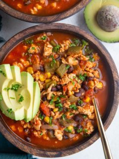 Two large wooden bowls of ground turkey taco soup with sliced avocado on top, ready to eat.