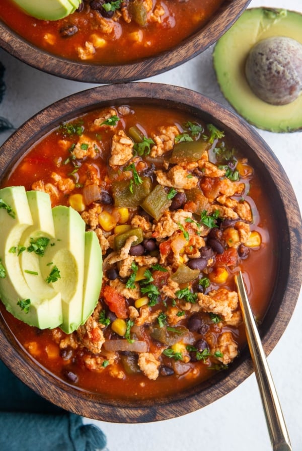 Two large wooden bowls of ground turkey taco soup with sliced avocado on top, ready to eat.