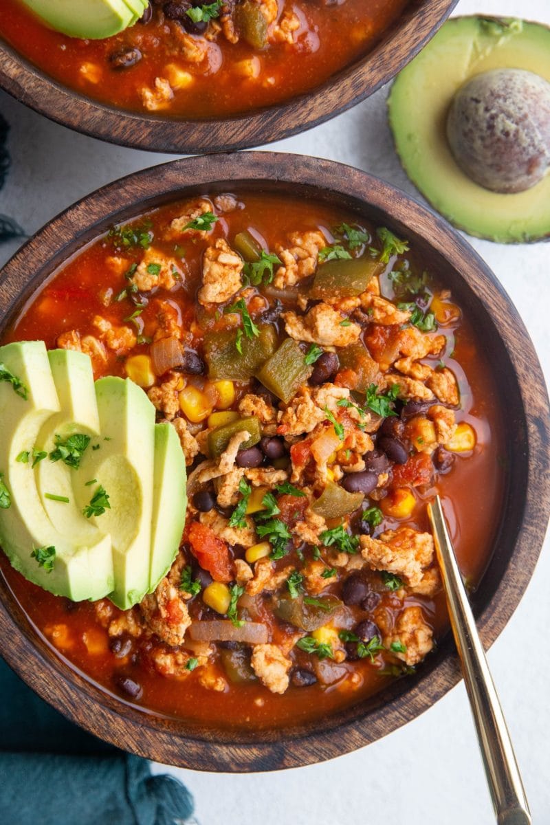 Two large wooden bowls of ground turkey taco soup with sliced avocado on top, ready to eat.