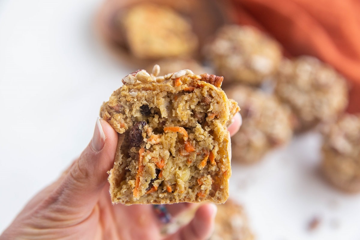 Horizontal photo of hand holding a morning glory muffin that has been sliced in half so you can see the inside.