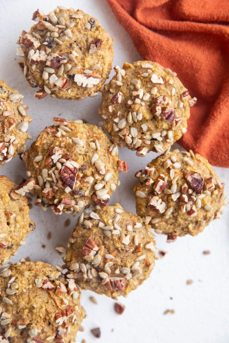 Top down photo of morning glory muffins on a white surface with a red napkin to the side.