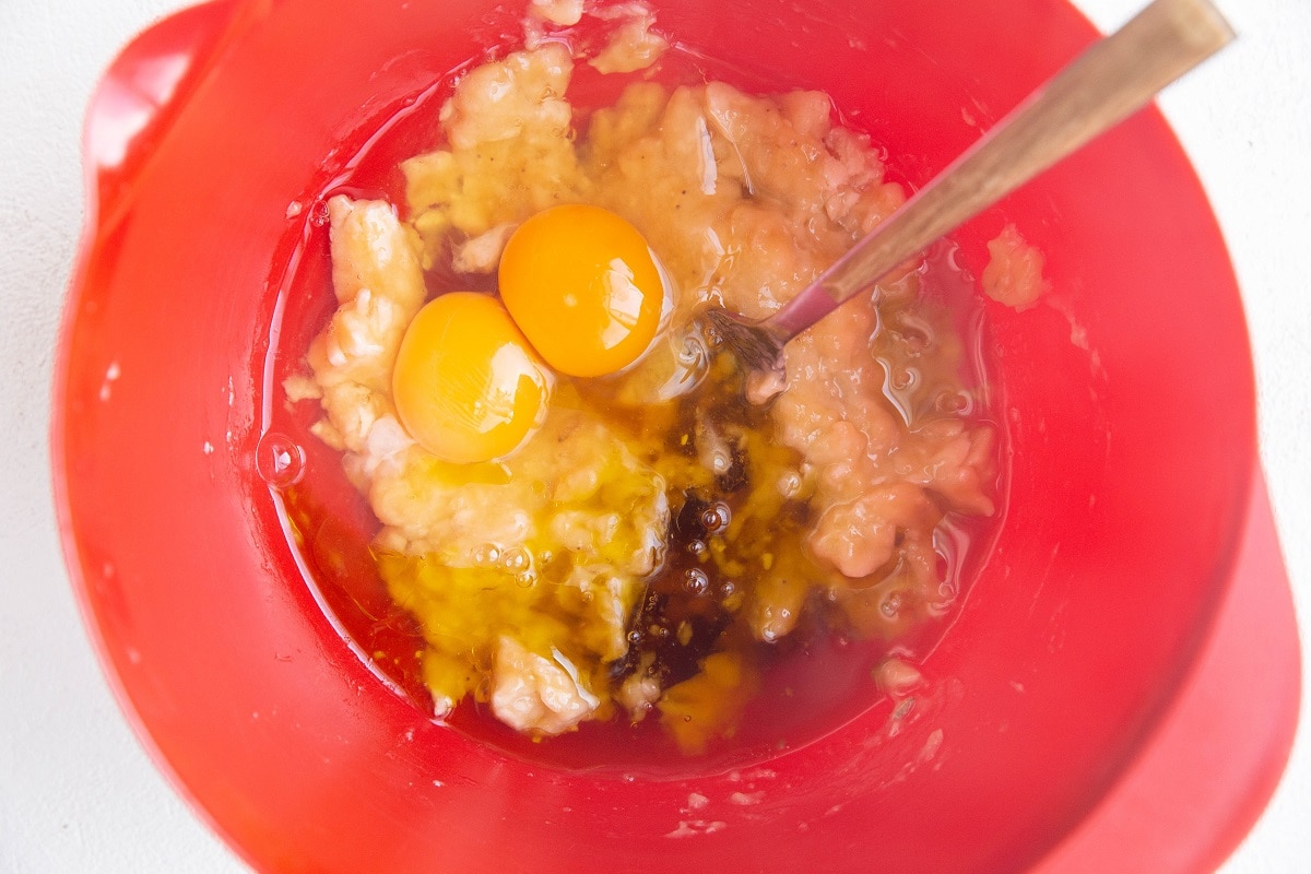 Mashed banana, eggs, oil and maple syrup (wet ingredients) in a mixing bowl, ready to be mixed together.