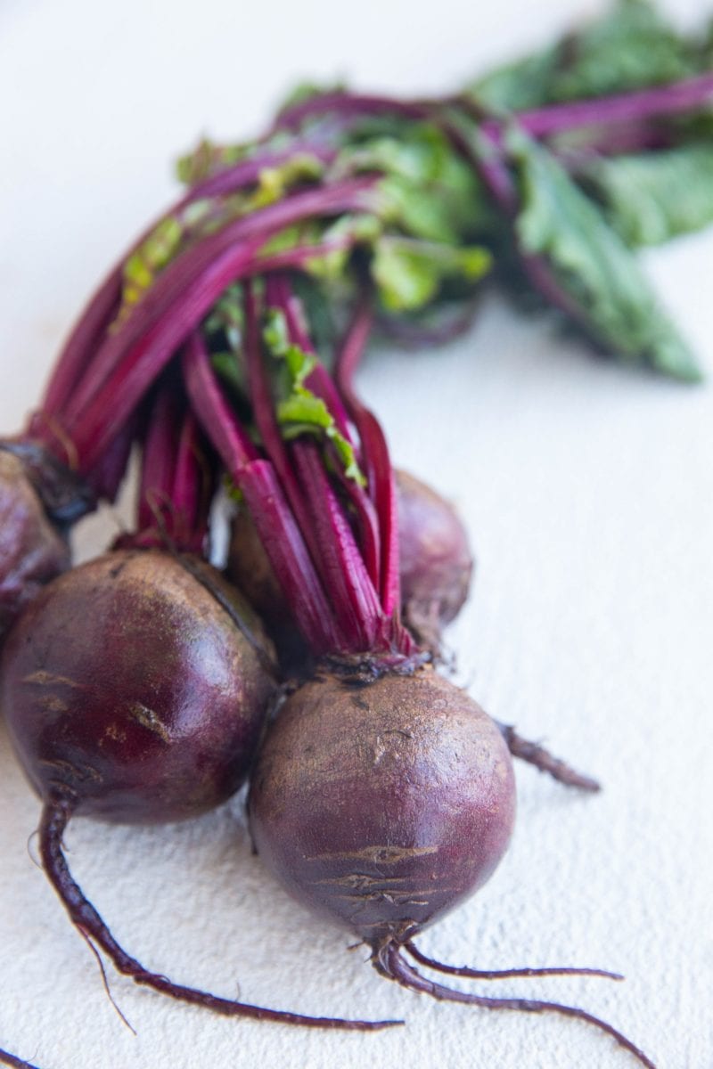 Bushel of beets with greens attached laying on a white background.