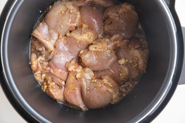 Raw marinated chicken thighs in an instant pot, ready to be cooked.