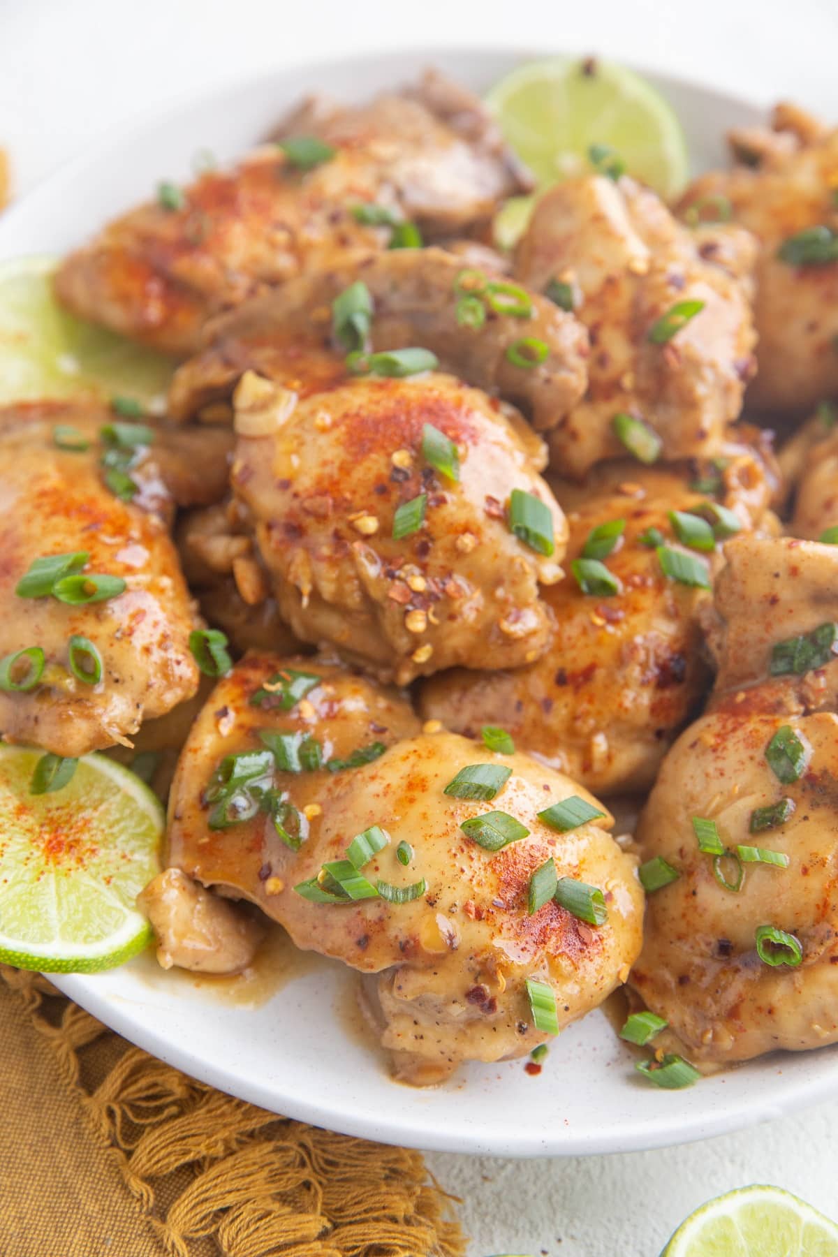 Plate of Asian-inspired chicken thighs, sprinkled with green onion with limes to the side.