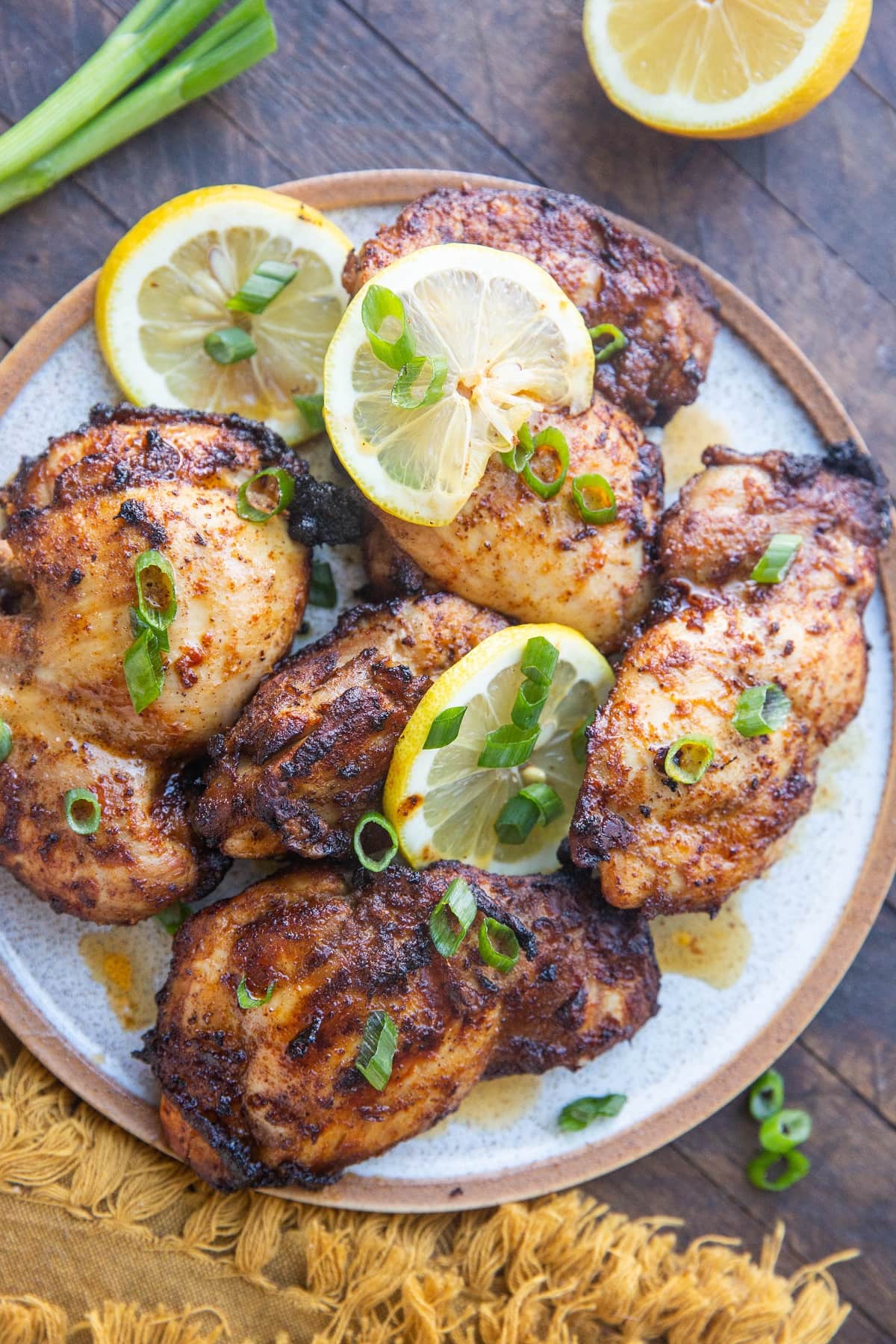 Top down plate of Mediterranean chicken sprinkled with green onions and slices of lemon on a rustic wooden background.