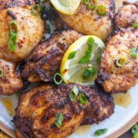 Close up plate of chicken thighs on a plate with green onions and lemon slices.