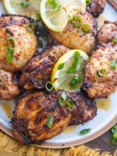 Close up plate of chicken thighs on a plate with green onions and lemon slices.