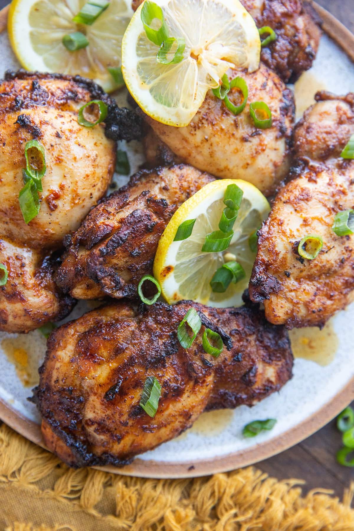 Close up plate of chicken thighs on a plate with green onions and lemon slices.