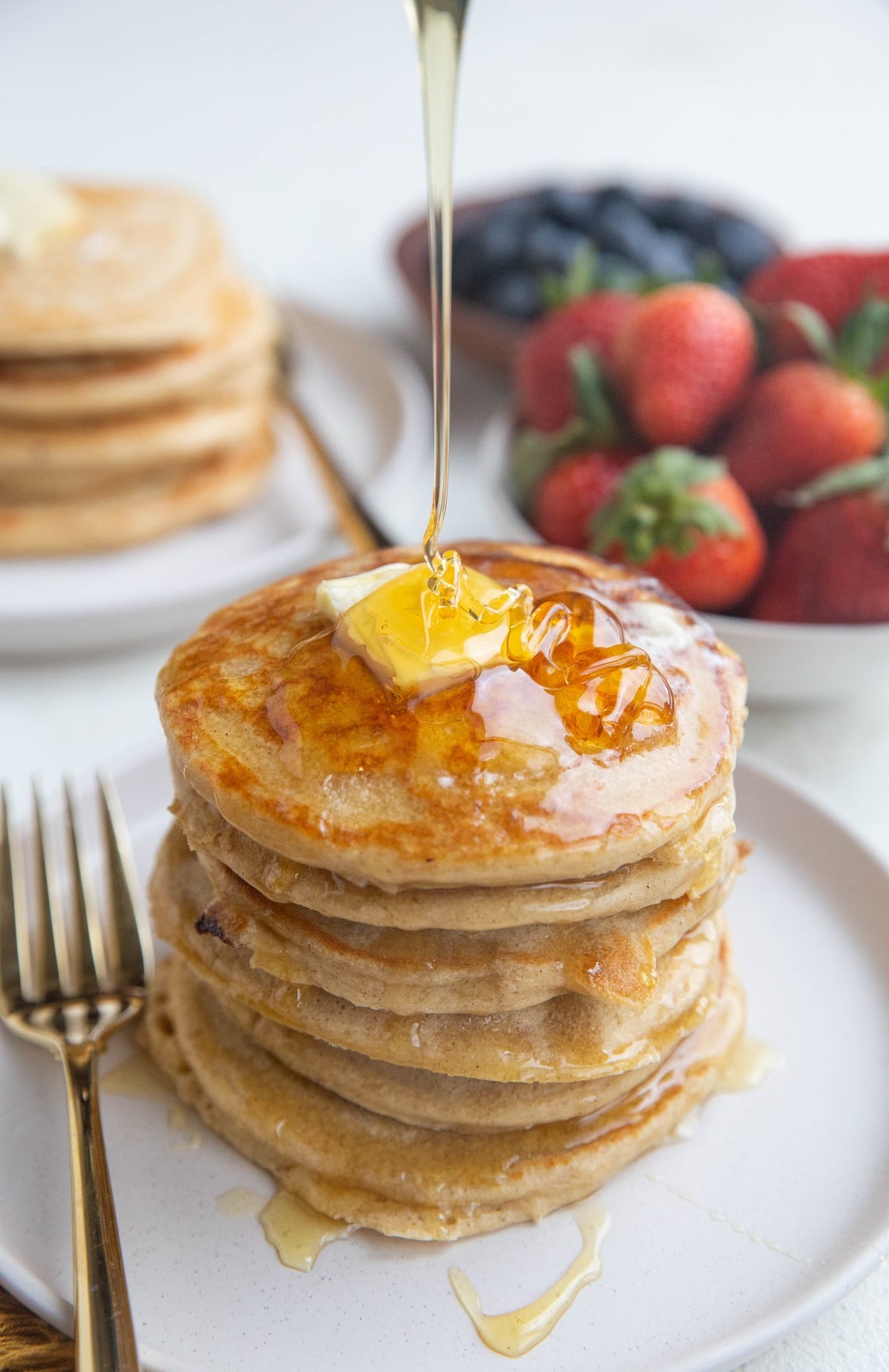 Stack of fluffy pancakes with butter on top with syrup being poured on the pancakes