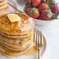 Angled shot of a stack of protein pancakes with syrup dripping down the side and butter on top.