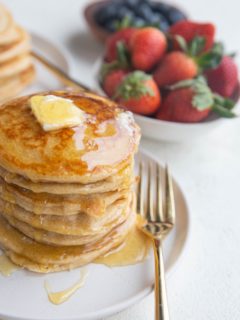 Angled shot of a stack of protein pancakes with syrup dripping down the side and butter on top.