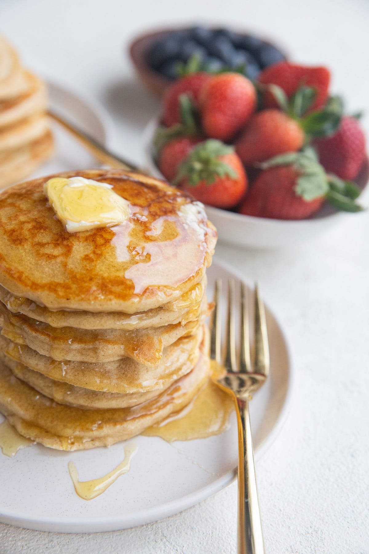 Angled shot of a stack of protein pancakes with syrup dripping down the side and butter on top.