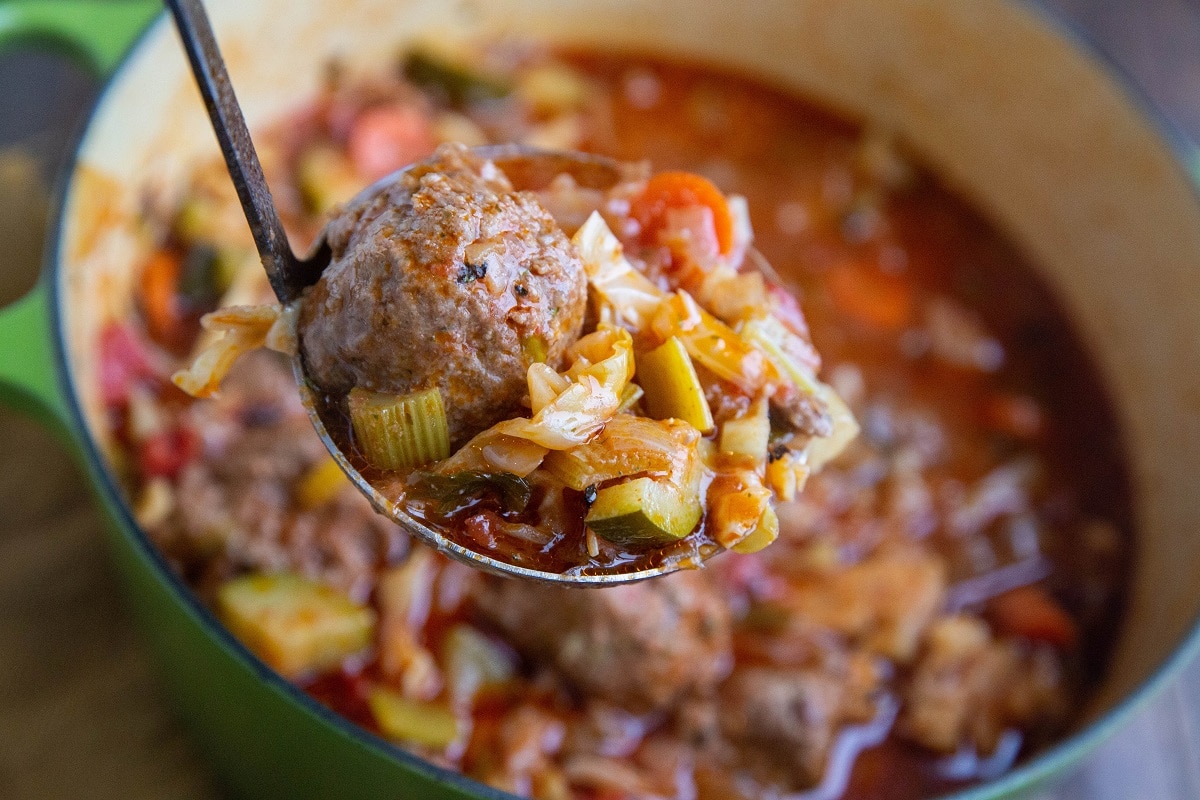 Horizontal image of pot of Sicilian meatball soup with a ladle scooping some of it out.