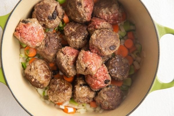 Meatballs on top of vegetables in a Dutch oven.