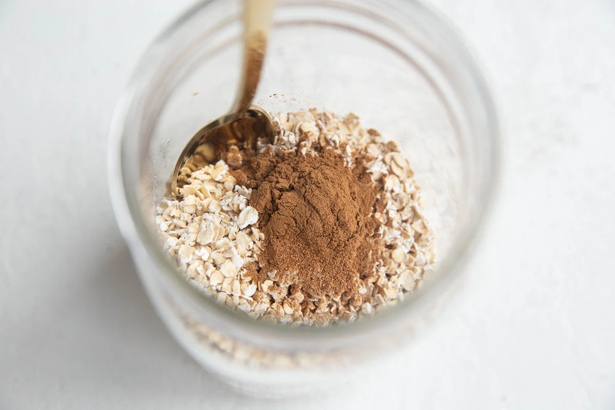 Oats and chai spice in a jar with a spoon, ready to be turned into overnight oats.