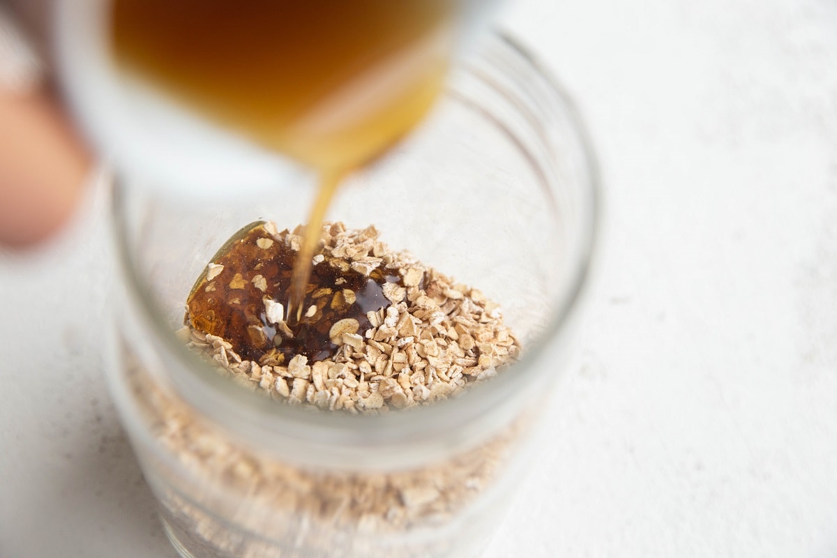 Pure maple syrup being poured into a large jar full of oats.