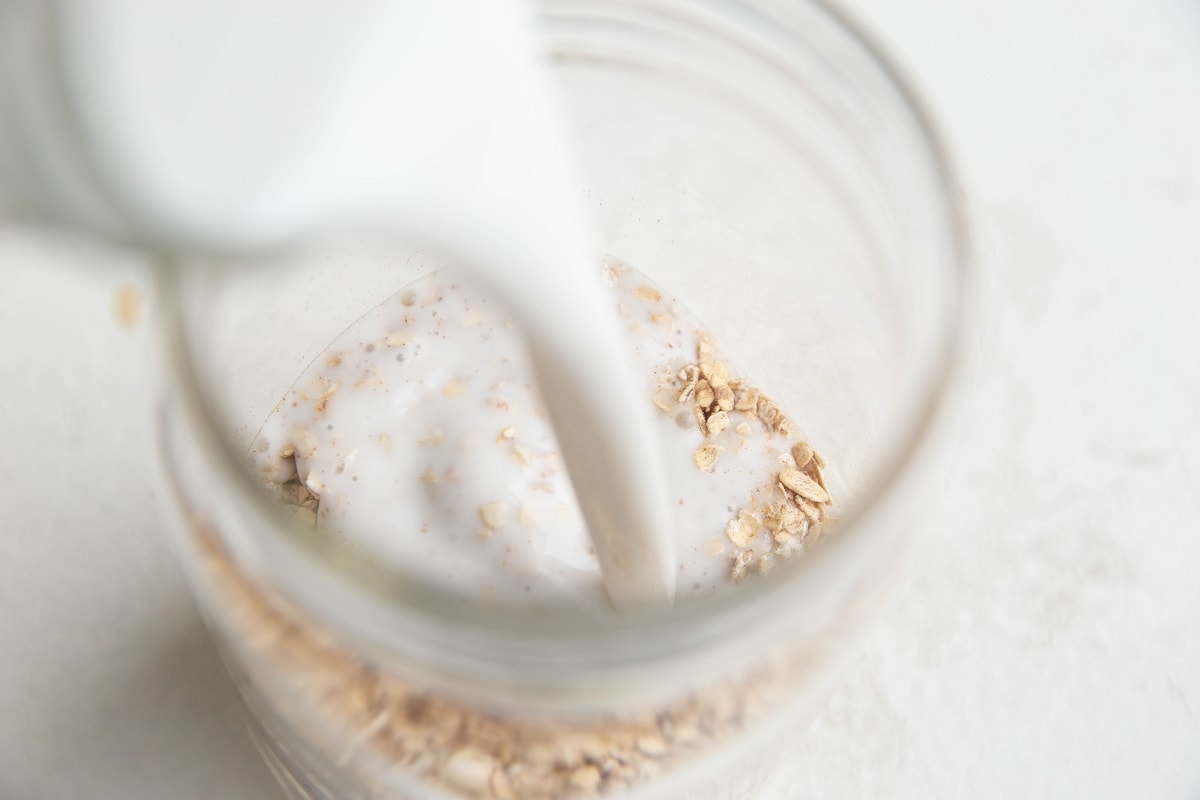 Full-fat canned coconut milk being poured into the jar of oats.