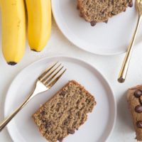 Top down photo of two white plates of slices of banana bread with golden forks, ready to eat.