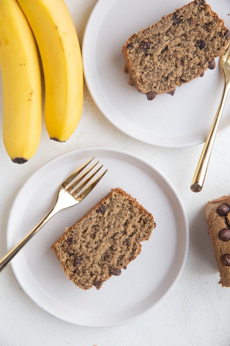 Top down photo of two white plates of slices of banana bread with golden forks, ready to eat.