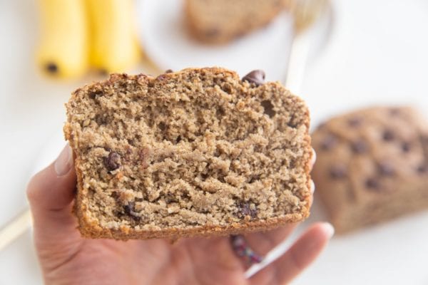 Horizontal photo of a hand holding a slice of banana bread so you can see the moist inside.