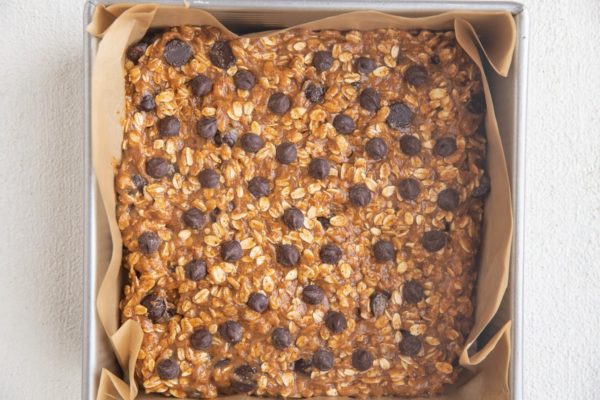 Square pan lined with parchment paper with cookie dough mixture pressed into an even layer.